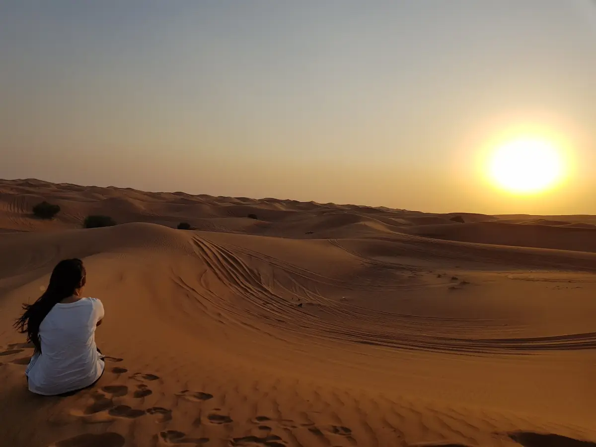 Eine Besucherin beobachtet auf einer Wüstensafari bei Dubai den Sonnenuntergang über den Dünen