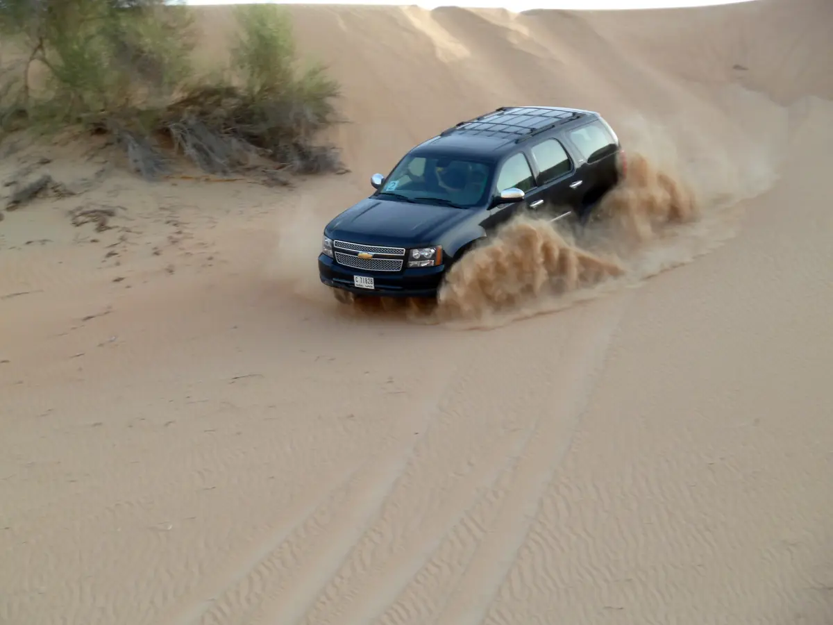 An SUV throwing up sand while driving down a dune near Dubai